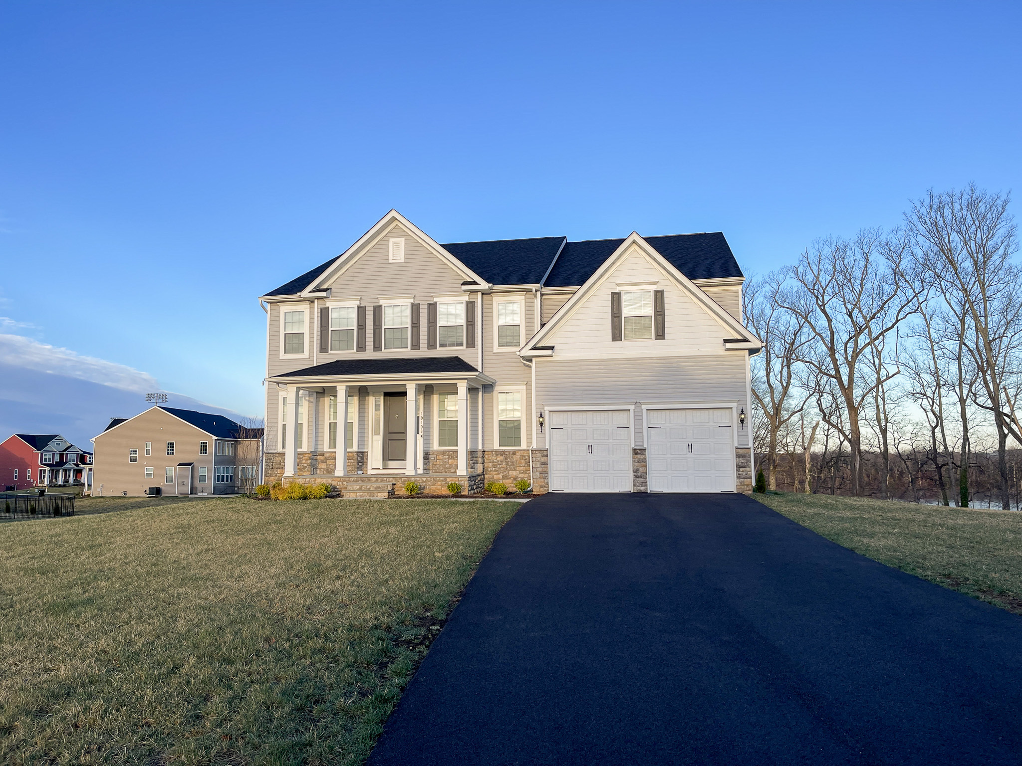 Two‑story gray suburban home with white trim, double garage, and a long paved driveway on a clear day belonging to Sponsored Residential Provider Homaira Yazdani in Fredericksburg, Virginia.