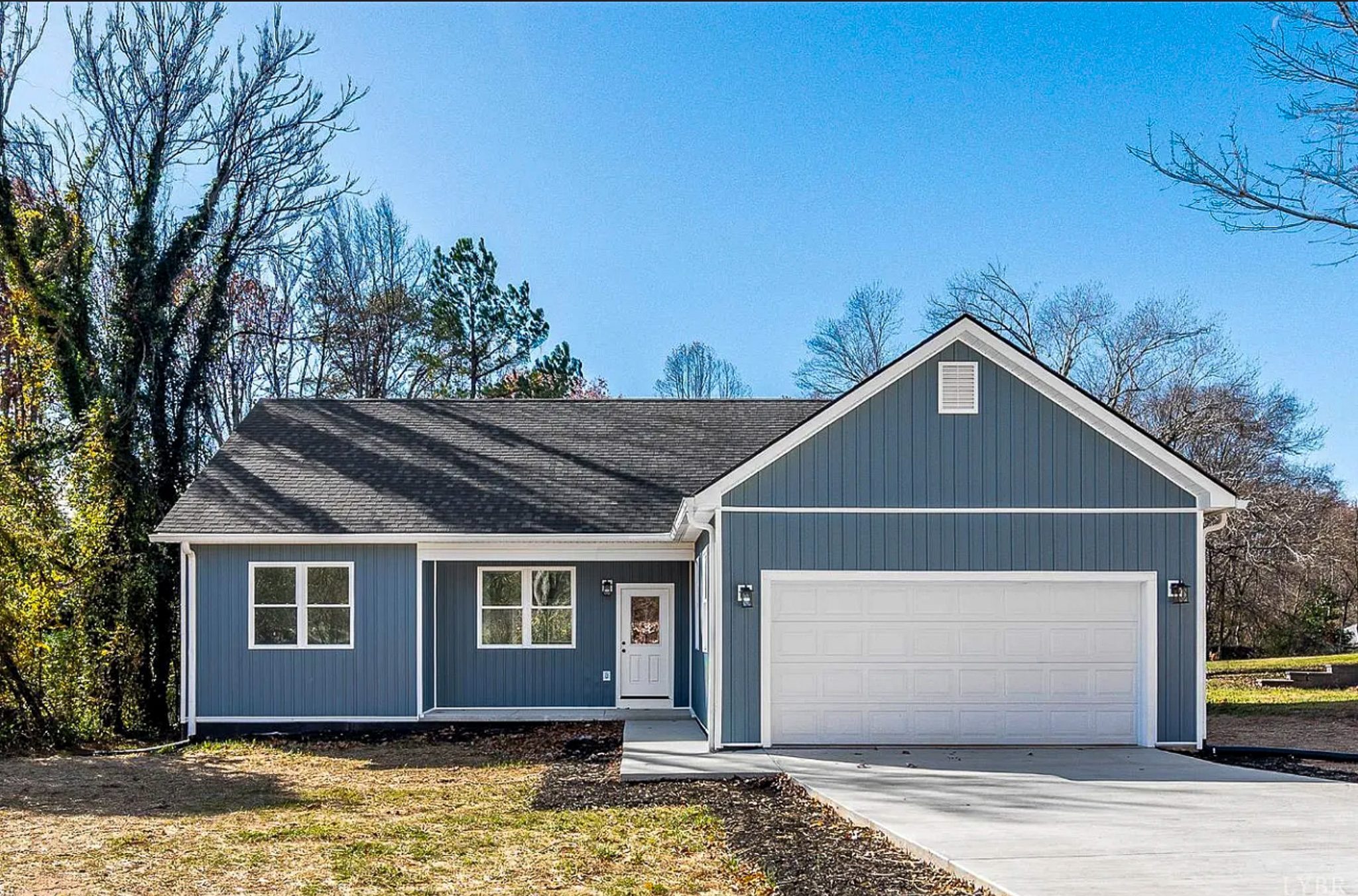 Single-story blue house with white trim, a two-car garage, and a concrete driveway under a clear blue sky belonging to Sponsored Residential Provider Angie Elcox in Madison Heights, Virginia.