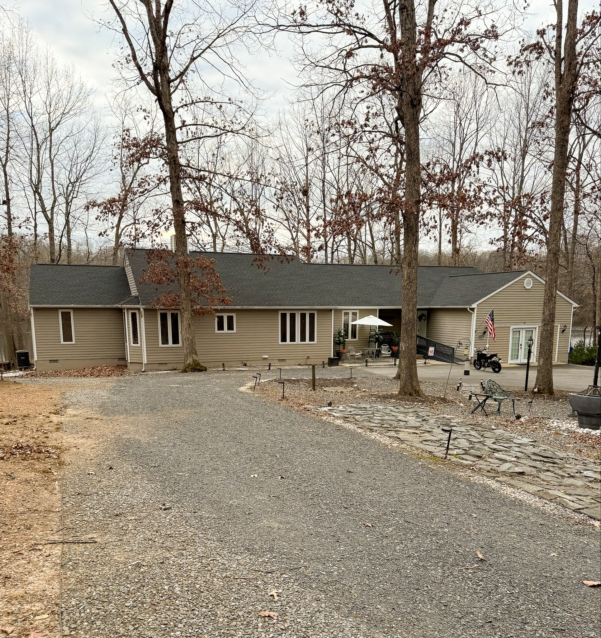 Long, single-story tan house with a gravel driveway, leafless trees, and a carport on the right side in a wooded setting belonging to Group Home Provider Ana Garcia in Spotsylvania, Virginia.