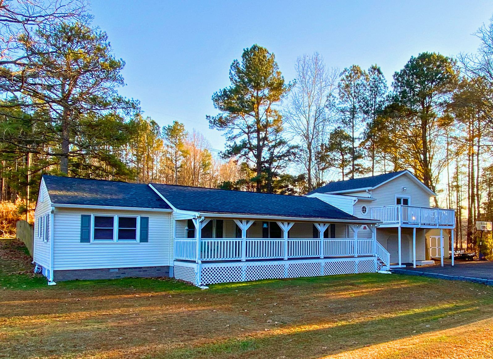 Single-story light blue house with a wraparound porch on a grassy property bordered by tall trees in warm golden sunlight belonging to Sponsored Residential Providers Bradley and Andrea Smith in Richmond.