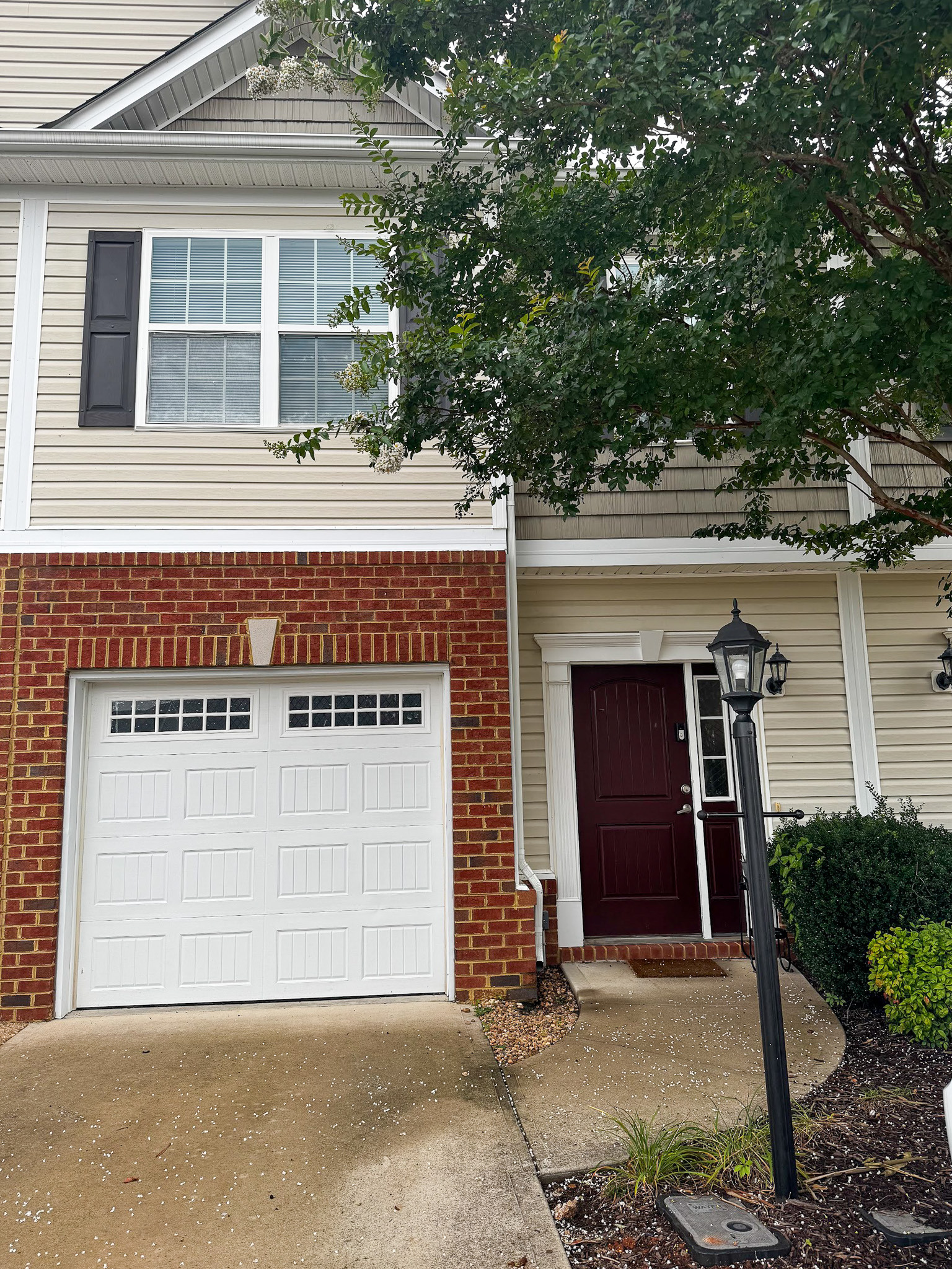 Brick townhouse exterior with a front porch, garage, and a tree partially obscuring the entryway belonging to the home of Sponsored Residential provider Cynthia Kimbrough-Mabry in Chester, Virginia