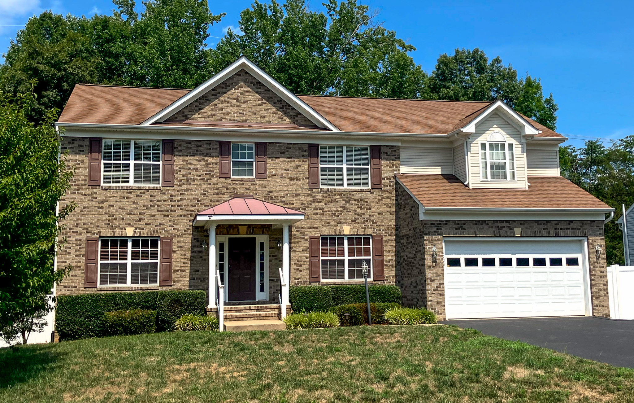 Two‑story brick house with white trim, a covered front entry, and an attached two‑car garage in Fredericksburg, Virginia which is an agency-operated Group Home with 24/7 awake staff.