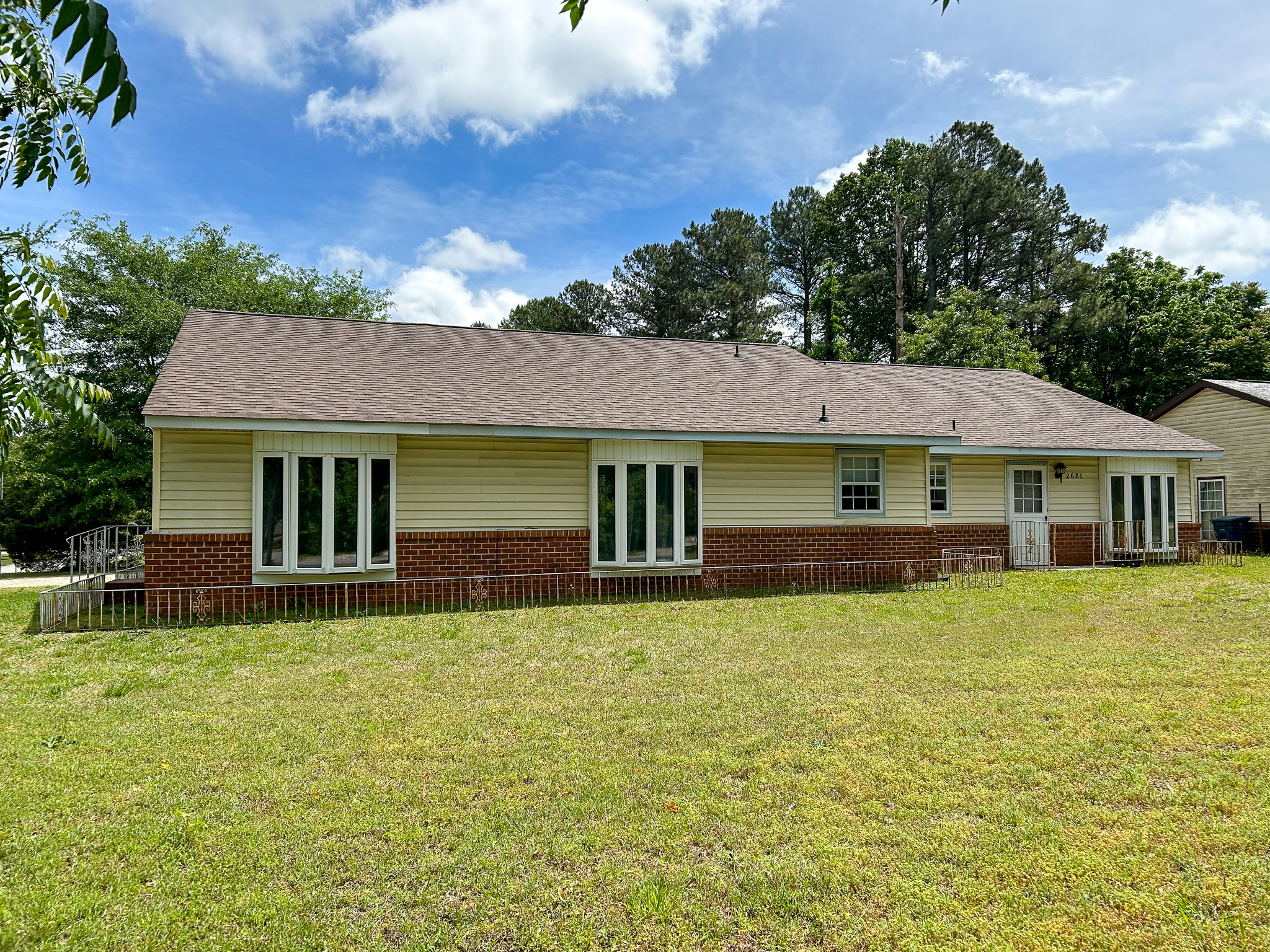 A long one‑story house with tan siding, red brick accents, multiple tall windows, and a large grassy backyard belonging to Group Home Provider William Harper in Prince George, Virginia.