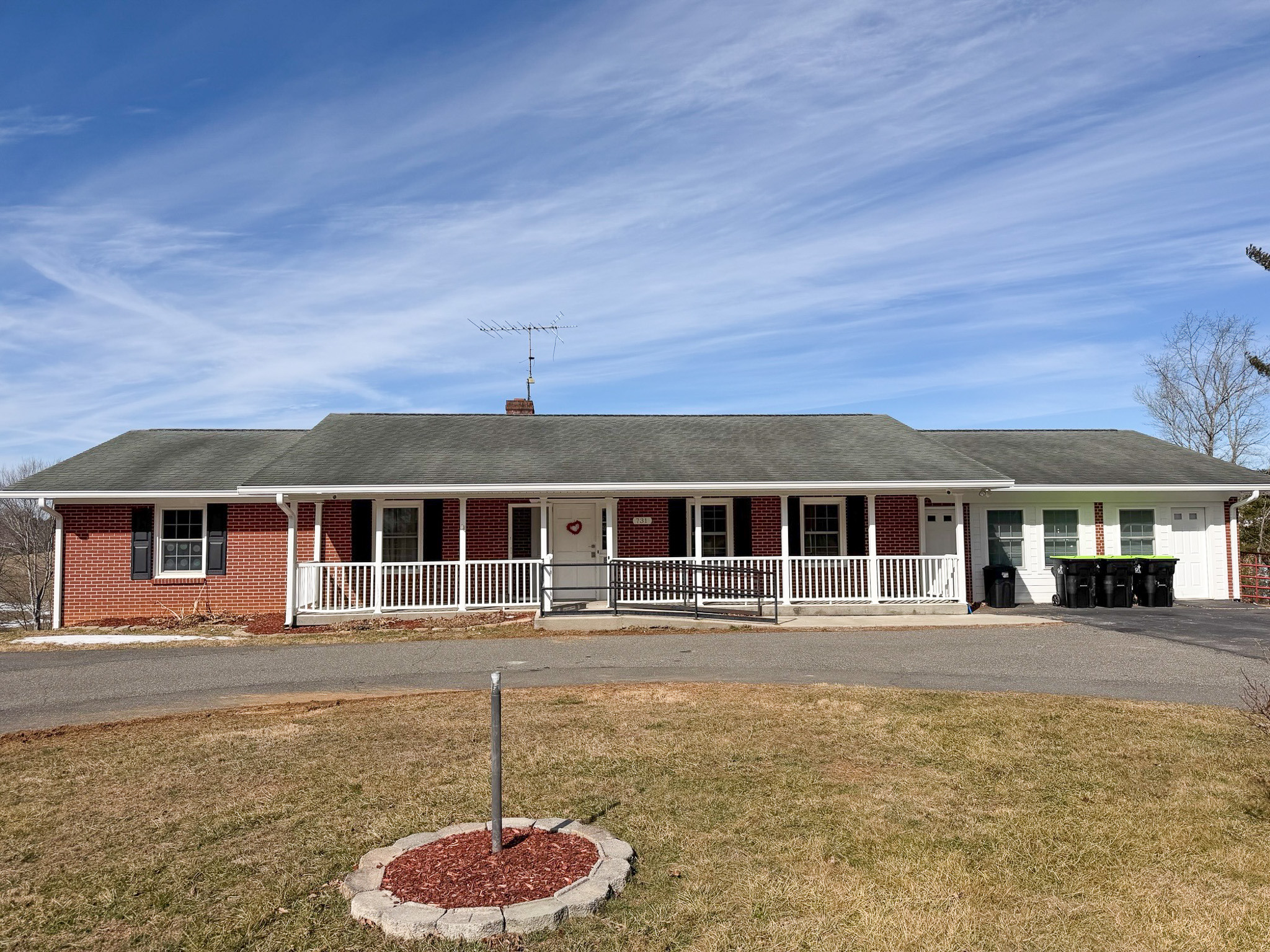 Single-story brick Wall Residences Agency-Run Group Home with a long front porch, white railing, and attached garage, set under a blue sky with light clouds.