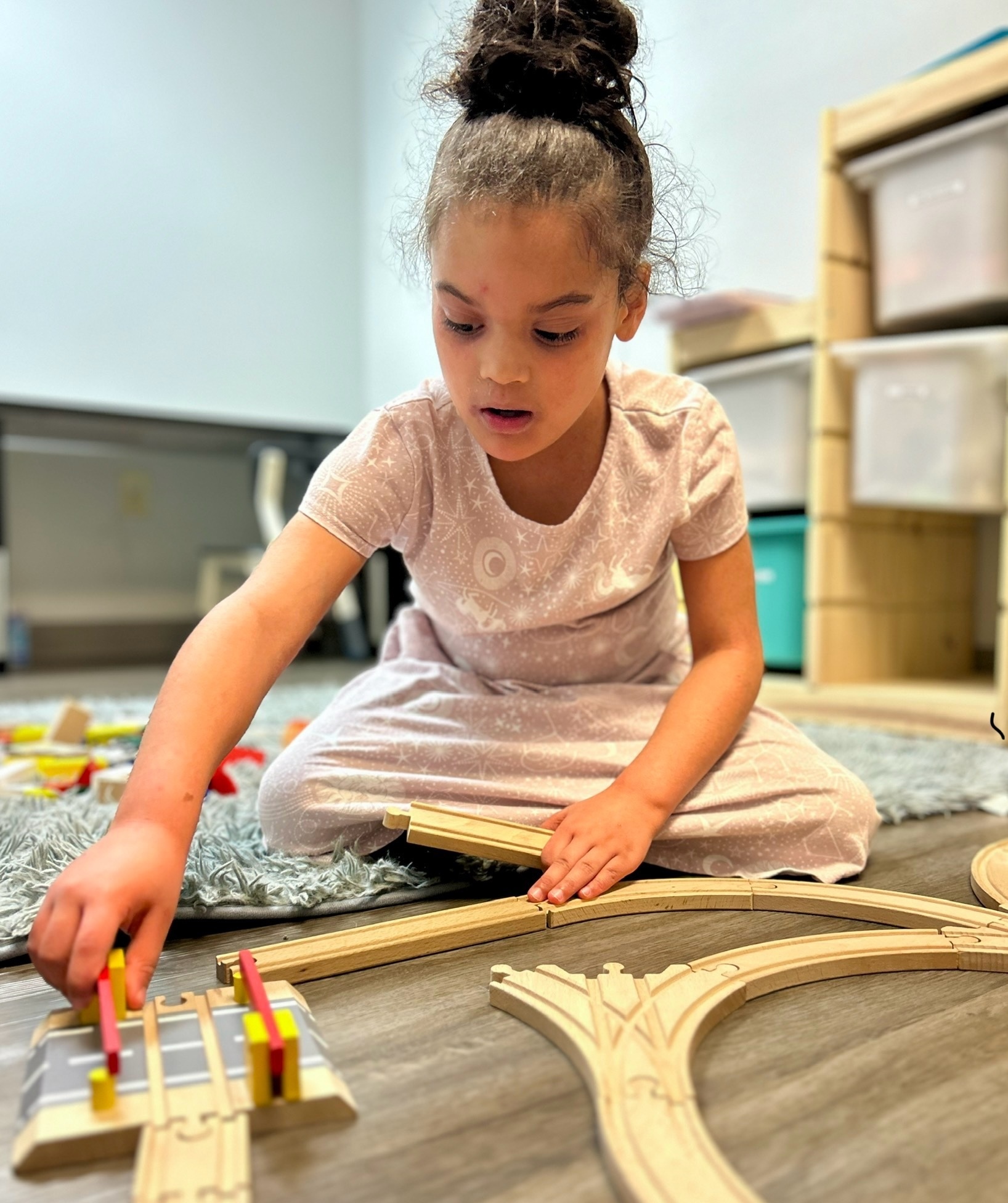 A young girl sitting on the floor of the Wall ABA Center playing with toy trains and tracks.