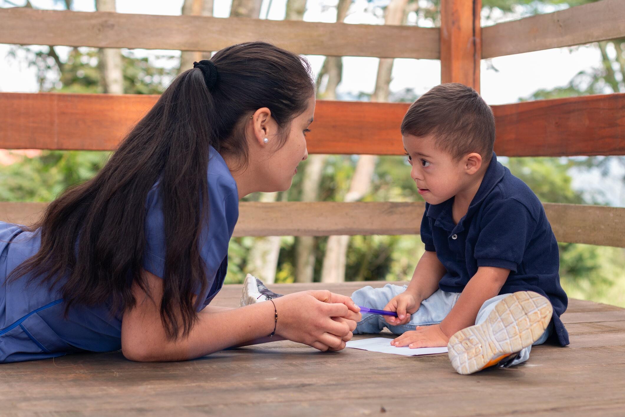 Instructor with a young boy drawing on paper