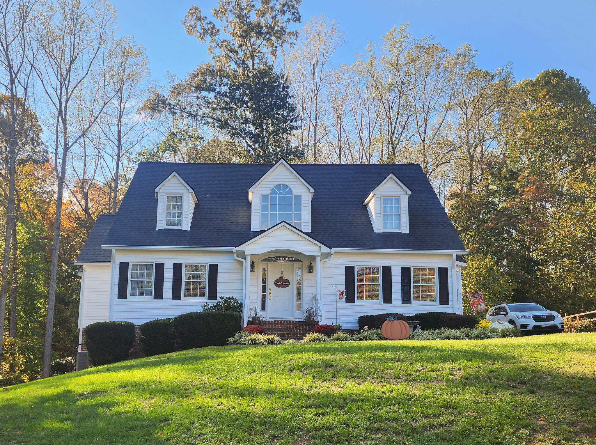 White two-story home with dormer windows, black shutters, and a grassy front yard surrounded by trees belonging to Sponsored Residential Providers Lisa and Randy Williamson in Lynchburg, Virginia.