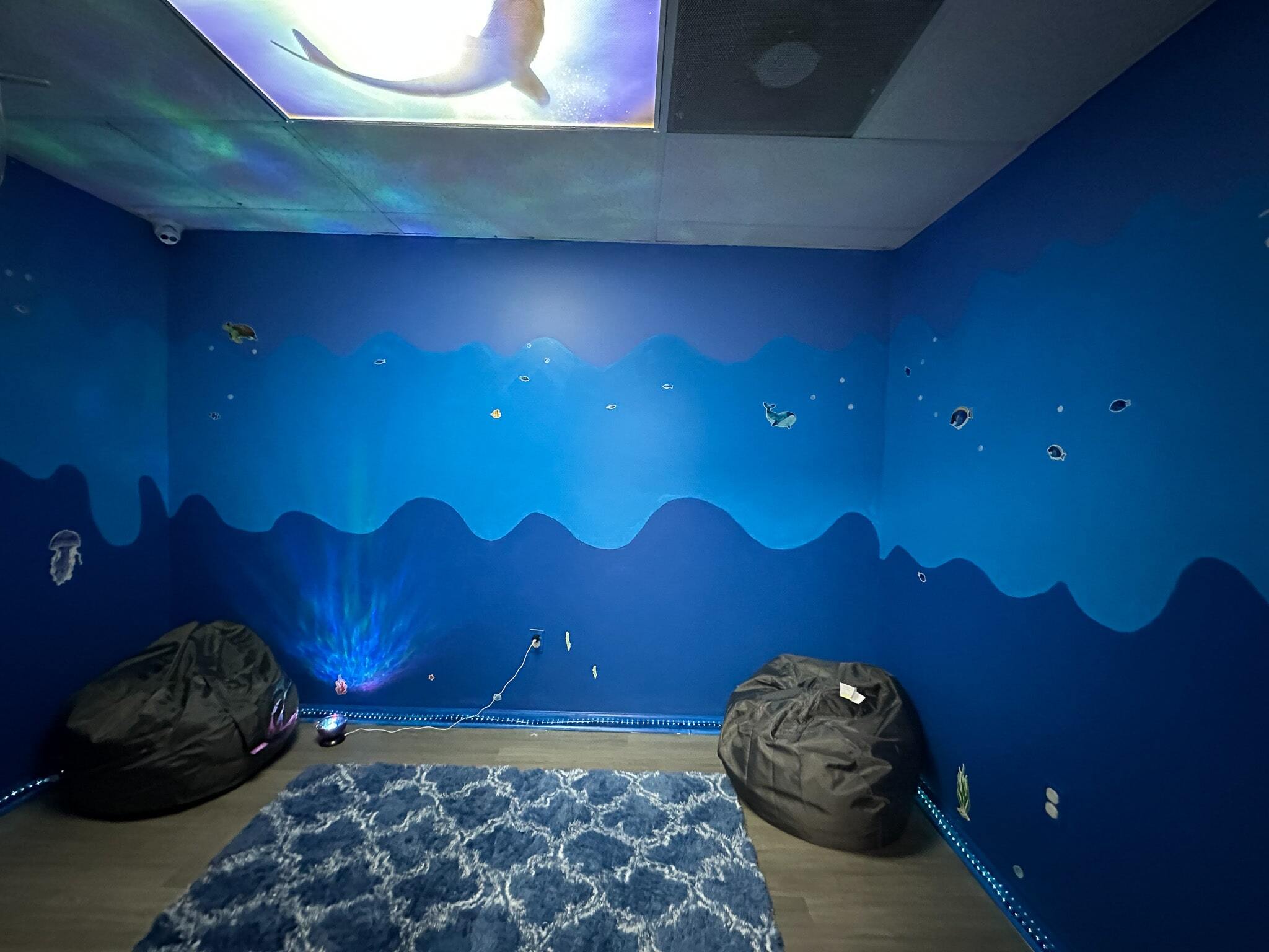 Ocean themed room painted in shades of blue with two bean bag chairs, a carpet, and a light projector