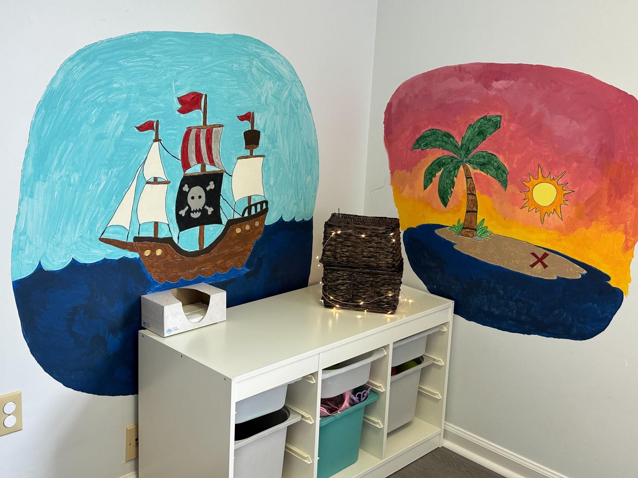 Corner of a room in the Salem ABA Center with drawers and two painted murals, one of a pirate ship and one of an island with treasure