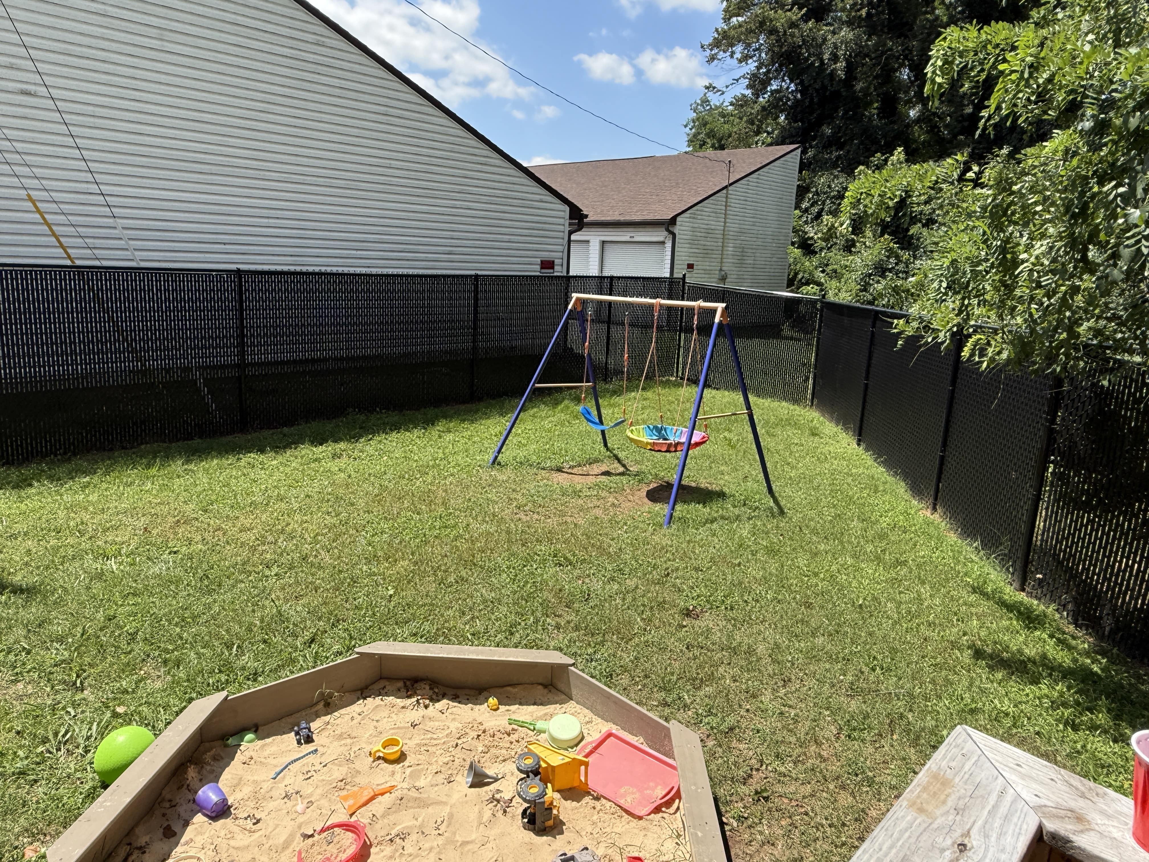 Outdoor area of the ABA Center with a swingset and sandbox filled with toys on a sunny day