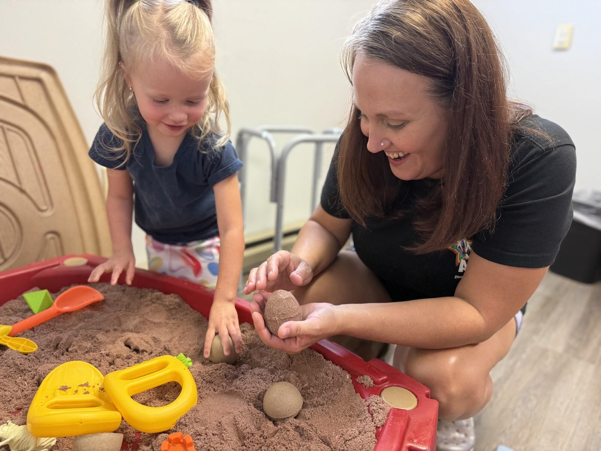 A young girl and clinician playing in a sandbox at the ABA center